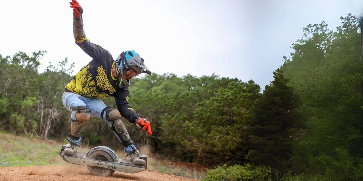 Person riding a onewheel on a dirt path with trees in the background